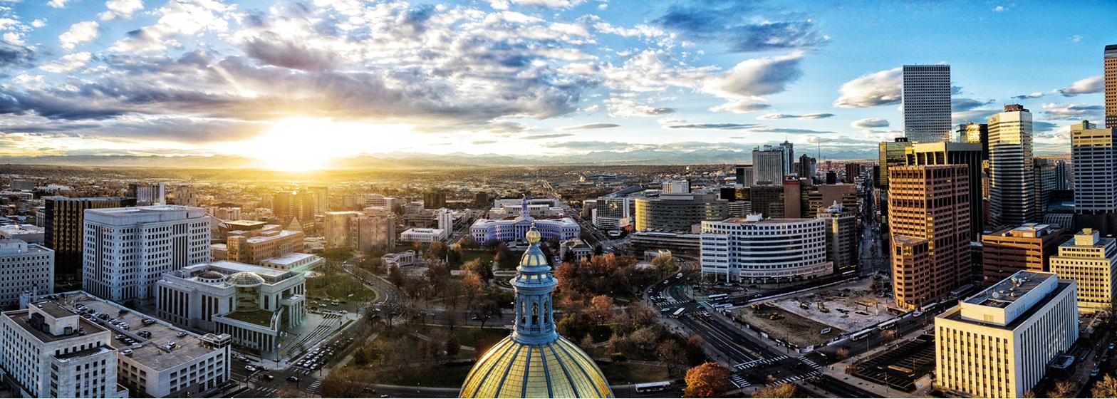 Aerial panoramic view of downtown Denver at sunset with the State Capitol dome in the foreground and Rocky Mountains on the horizon